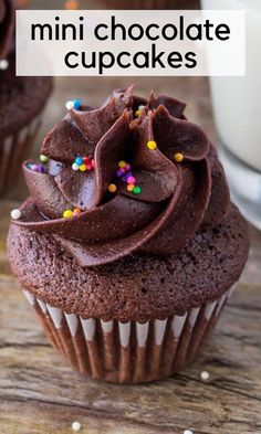 chocolate cupcakes with chocolate frosting and sprinkles are on a wooden table