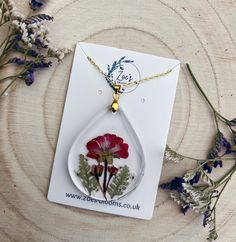 a flower in a tear shaped glass pendant on a card next to some wildflowers