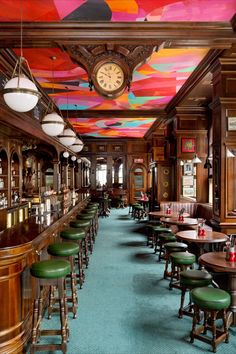 the interior of a restaurant with many tables and stools in front of a clock