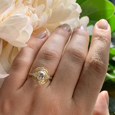 a woman's hand with a gold ring on it and flowers in the background