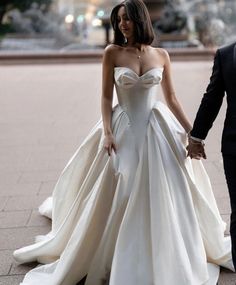 a bride and groom holding hands walking down the street