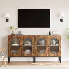 a television mounted on the wall above a wooden cabinet with glass doors and metal handles