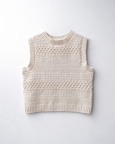 a white knitted sweater hanging on a wall with the top portion of it showing an openwork pattern