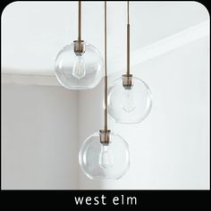 three clear glass globes hanging from a ceiling fixture with the words west elm above them