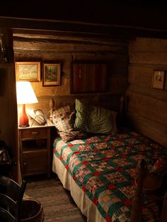 a bed sitting next to a night stand in a room with wooden walls and flooring