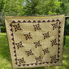 a quilt hanging on a clothes line in the grass with trees in the back ground