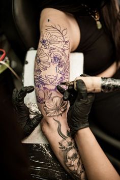 a woman sitting in a chair with tattoos on her arm and leg, holding a paintbrush