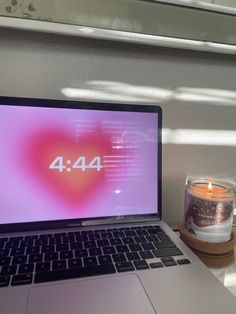 an open laptop computer sitting on top of a desk next to a candle and cup