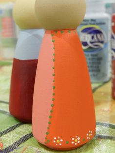 two wooden peg dolls sitting on top of a table next to cans of sodas