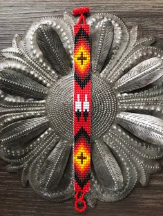 a red and yellow beaded bracelet sitting on top of a wooden table next to a metal object