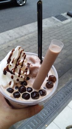 a person holding up a cup with ice cream and chocolate on the top, in front of a city street