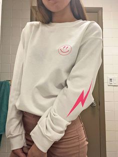 Bring happiness wherever you go with this super trendy lightning bolt smiley face crewneck sweatshirt! Featuring a bold, simple, smiley face graphic in hot pink and lightning bolts on each sleeve, this piece is perfect to finish off your trendy, oversized look! It is preppy, and adorable! Makes a great gift for a friend, or for yourself! Please note: This item features heat transferred plastisol graphics. Printed on a soft, cotton-poly blend Gildan sweatshirt. SIZING: Our sweatshirts are unisex Casual Smiley Face Winter Tops, Casual Winter Tops With Smiley Face, Trendy Crew Neck Sweatshirt, Trendy Smiley Face Sweatshirt For Fall, Trendy Smiley Face Tops For Fall, Long Sleeve Smiley Face Top For Fall, Trendy Fall Sweatshirt With Smiley Face, Trendy Fall Smiley Face Tops, Trendy Fall Tops With Smiley Face