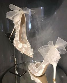 two pairs of shoes with white lace and bows on display in a glass case at a museum