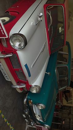 an old red and white car is parked in a garage next to another green car