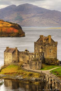 an old castle sitting on top of a small island next to the ocean with mountains in the background