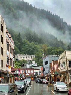 cars parked on the side of a road in front of buildings with mountains in the background