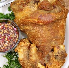 a white plate topped with meat and vegetables next to a bowl of corn on the cob