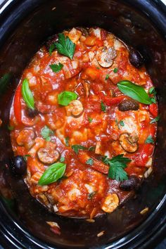 a slow cooker filled with food and garnished with fresh basil leaves on top