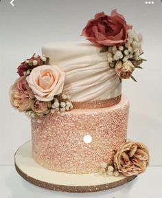 a three tiered wedding cake with flowers on it's side and gold sequins around the edges