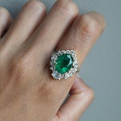 a woman's hand holding a ring with a green stone surrounded by white diamonds