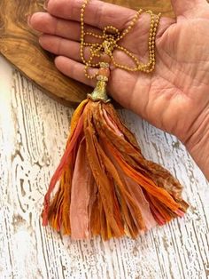 This listing is for one recycled sari silk tassel as shown. It comes with a 30" gold tone ball chain as pictured. Lot #17 Color: Shades of Orange Length: 6 1/2" The ornate lead free pewter bead cap is topped with Agate gemstone and crystal roundels for a beautiful statement piece.  Wear it on the included ball chain or your own chain for a romantic bohemian look, or use it in one of your own creations. Our Bohemian sari silk tassels are uniquely handmade and put together with Recycled Sari Silk, Bohemian Gold Tassel Necklace, Bohemian Gold Tassel Necklace As Gift, Bohemian Gold Tassel Necklace For Gift, Gold Tassel Necklaces For Festival, Gold Tassel Necklace For Festivals, Gold Bohemian Tassel Necklace Adjustable, Adjustable Gold Bohemian Tassel Necklace, Handmade Adjustable Gold Tassel Necklace, Gold Tassel Necklace With Fringe For Gift