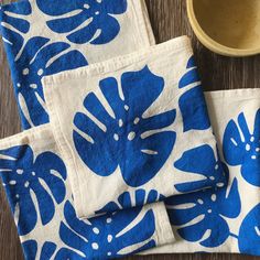 three blue and white napkins sitting on top of a wooden table next to a bowl