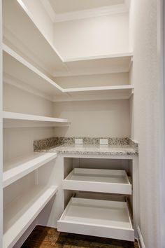 an empty walk in closet with white shelving and granite counter tops on the shelves