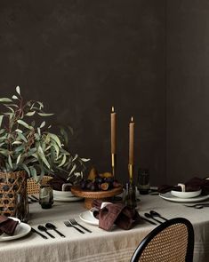 the table is set with plates, silverware and candles in front of a potted plant