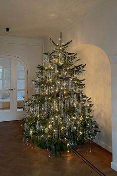 a christmas tree is lit up in the middle of a room with wood flooring