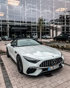 a white mercedes sports car parked in front of a large glass building with lots of windows