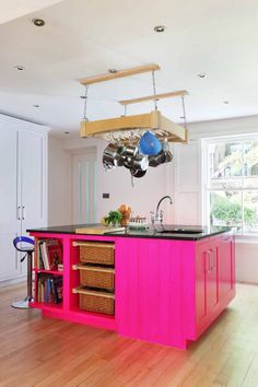 a kitchen with pink island in the middle of it and hanging pots on the rack