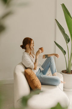 a woman sitting on top of a white couch next to a potted plant