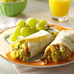 two burritos on a plate with grapes and orange juice