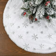 a white christmas tree skirt with pine cones and red berries on it, sitting on top of a wooden table