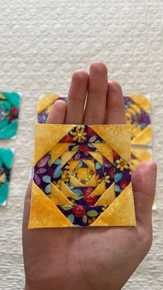 a hand holding an origami piece in the shape of a flowered square