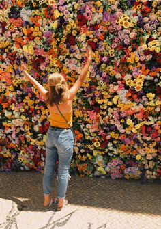 a woman standing in front of a flower wall with her arms up and hands raised