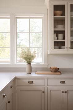 a kitchen with white cupboards and counter tops next to a vase filled with flowers