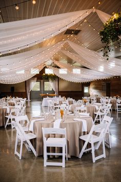 a banquet hall with tables and chairs covered in white draping, decorated with lights