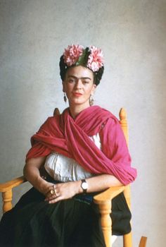 an old photo of a woman sitting in a chair wearing a pink shawl and flowers on her head