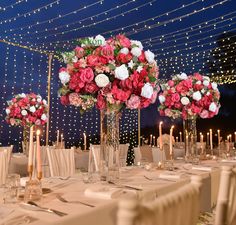 there are many tall vases with flowers on the tables at this wedding reception in front of string lights