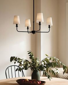 a dining room table with a bowl of fruit on it and four lights hanging from the ceiling