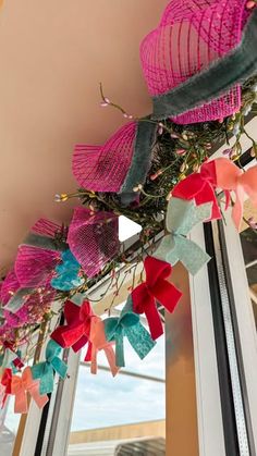 some pink and blue paper flowers hanging from the ceiling in front of a window sill