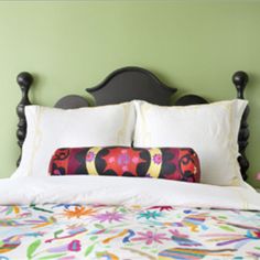 a bed with white pillows and colorful comforter on it's headboard in a green room