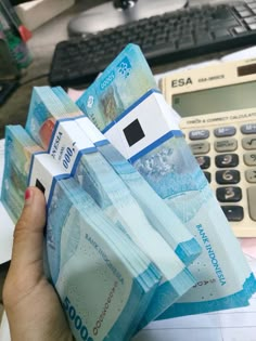 a person is holding some money in front of a calculator and computer keyboard