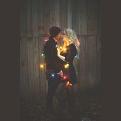 two people standing next to each other in front of a fence with christmas lights on them