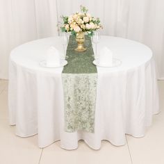 a white table topped with a vase filled with flowers next to two empty wine glasses