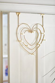 a heart shaped metal decoration hanging from a white door with two hooks on it's side