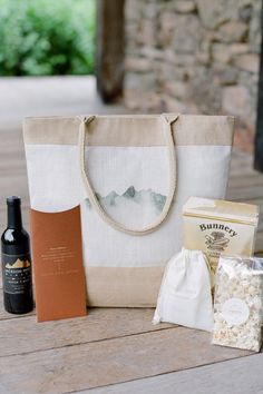 a wine bottle, bag, and other items are sitting on a wooden table outside