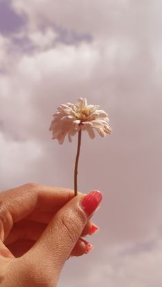 a woman's hand holding a flower in front of a cloudy sky