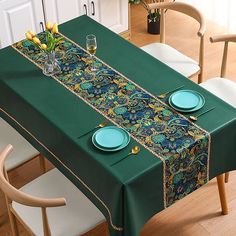 a green table cloth with blue plates and flowers on it is sitting in front of two chairs